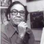 A imagem é um retrato em preto e branco de um homem de meia-idade ou idoso, de pele clara, olhando diretamente para a câmera. Ele tem cabelo escuro e ondulado, e usa óculos de armação escura e retangular. Ele veste uma camisa social de manga comprida e colarinho aberto. Sua mão direita está apoiada sob o queixo, com os dedos fechados. O fundo é um ambiente interno com elementos artísticos. À esquerda e acima, há quadros com pinturas claras e formas orgânicas, e à direita, outra pintura ou obra de arte mais escura é visível. A iluminação é suave.