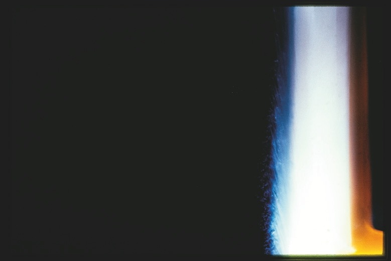 Descrição da imagem: Fotografia horizontal colorida abstrata, com um fundo predominantemente escuro à esquerda e uma faixa vertical de luz à direita, em tons de azul, branco e laranja. A imagem, com a luz parecendo vir de uma fonte lateral, cria uma transição suave entre as áreas iluminadas e as sombras profundas. Fim da descrição da imagem.