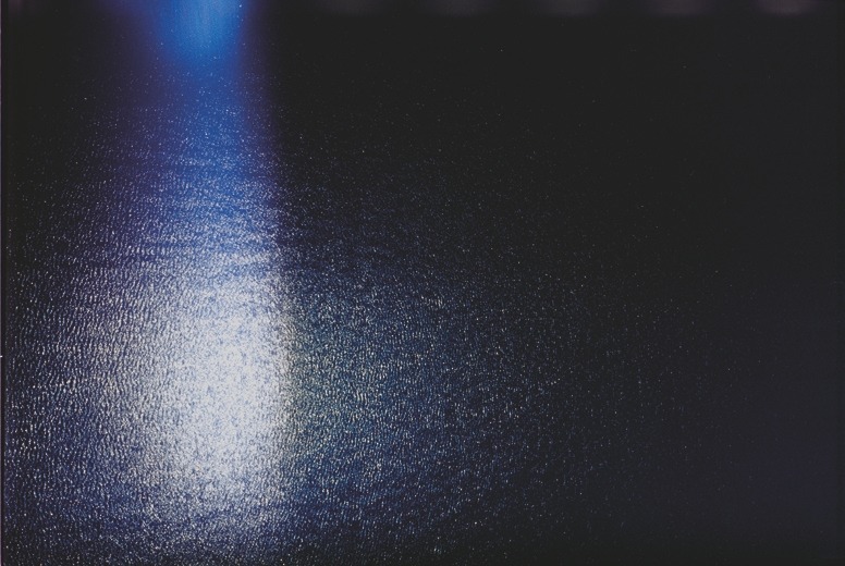 Descrição da imagem: Fotografia horizontal colorida de uma superfície de água. A luz solar, em tons de azul e braco, reflete suavemente na superfície ondulada, criando um brilho vertical que se estende da parte superior do lado esrquedo até o centro da imagem. Fim da descrição da imagem.