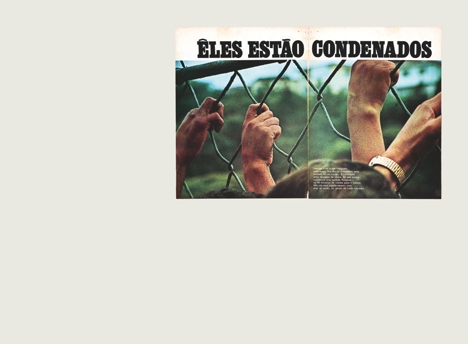 Descrição da imagem: Revista aberta com uma grande fotografia colorida que toma as duas páginas. Na parte superior, sobre uma faixa branca na horizontal, a frase “ELES ESTÃO CONDENADOS” em letras pretas garrafais. Abaixo, na foto, quatro mãos de pele branca agarram uma grade de alambrado. Na parte inferior da imagem, o topo de duas cabeças, sobre uma delas, à direita, um texto muito pequeno em letras brancas com os dizeres: "George Love é um fotógrafo americano. Um dia se interessou pelo futebol, foi ao campo. E continuou indo, dezenas de vezes. Só que nunca assistiu a uma partida. Passava os 90 minutos de costas para o campo. Não viu uma jogada sequer, mas elas aí estão, no gesto de cada torcedor". Ao fundo, atrás da grade, está desfocado. Fim da descrição da imagem.