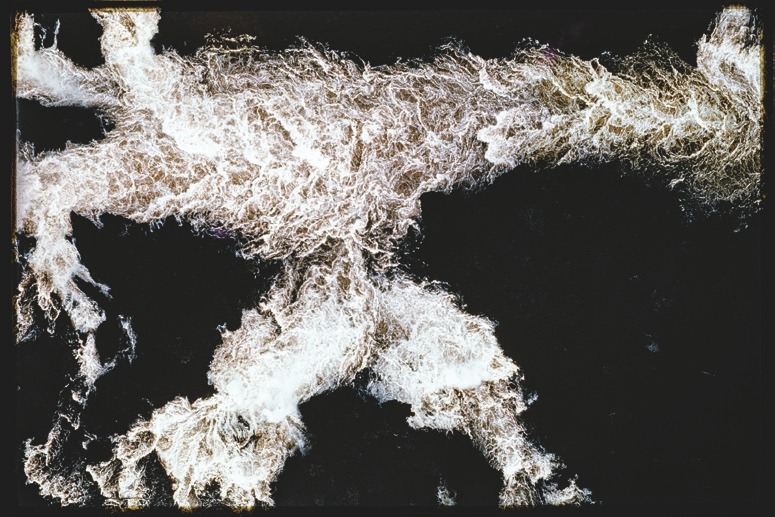 Descrição da imagem: Fotografia colorida horizontal. A imagem apresenta uma vista aérea de uma grande massa de água em movimento, criando um padrão caótico de ondas e espumas brancas sobre um fundo escuro. As águas turbulentas formam linhas e ramificações, lembrando galhos de uma árvore, com a espuma clara contrastando fortemente com o fundo. Fim da descrição da imagem.