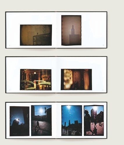 Descrição da imagem: Imagem colorida e horizontal. Três livros abertos são dispostos em uma superfície clara, mostrando suas páginas internas. O primeiro livro, na parte superior, exibe uma página com uma fotografia de um prédio em construção, à esquerda e uma imagem da silhueta de o topo de um prédio alto, à direita. O segundo livro mostra duas fotografias: à esquerda, uma sobreposição de cenas urbanas, que apararecem carros, retratos e faxadas de lojas, e à direita, uma imagem desfocada de luzes com móbiles pendurados em primeiro plano. O terceiro livro apresenta quatro fotografias verticais de cenas urbanas, mostrando silhuetas de pessoas e edifícios contra um céu azul e contro o sol. Fim da descrição da imagem.