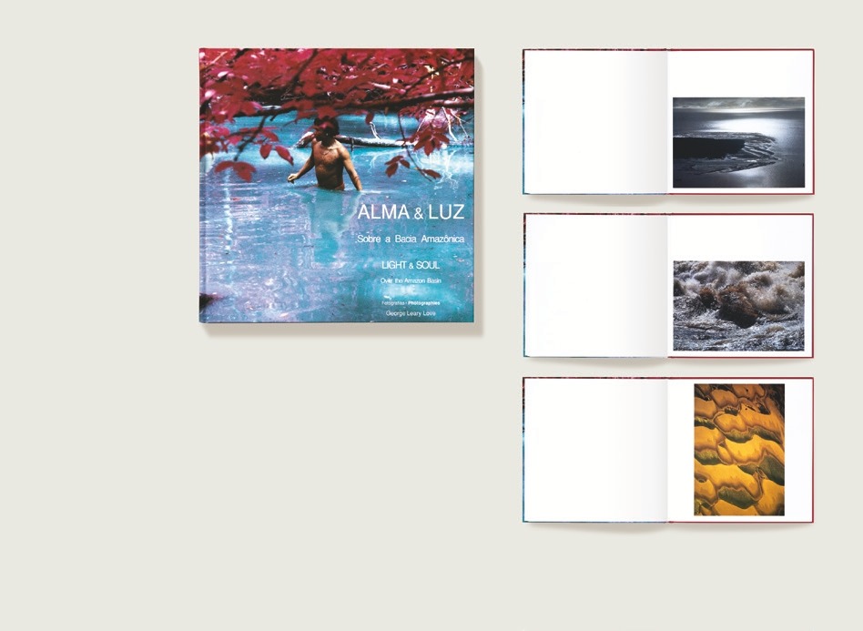 "Descrição da imagem: A imagem apresenta a capa e páginas internas do livro ""Alma & Luz: Sobre a Bacia Amazônica"". A capa, localizada à esquerda, mostra uma fotografia colorida de uma pessoa imersa até a cintura em águas azuladas, cercada por galhos de árvore com folhas vermelhas. O título ""ALMA & LUZ"" está centralizado na parte inferior da capa, acompanhado de textos em português e inglês, incluindo ""Sobre a Bacia Amazônica"" e ""Light & Soul: Over the Amazon Basin"". Abaixo do texto principal, há o crédito do fotógrafo, George Leary Love. À direita, três páginas abertas do livro são exibidas em sequência vertical. Cada página da direita contém uma fotografia colorida. A primeira mostra uma vista aérea de uma costa com águas escuras; a segunda apresenta um close-up de uma correnteza em um rio; a terceira retrata uma série de dunas de areia douradas. Fim da descrição da imagem."