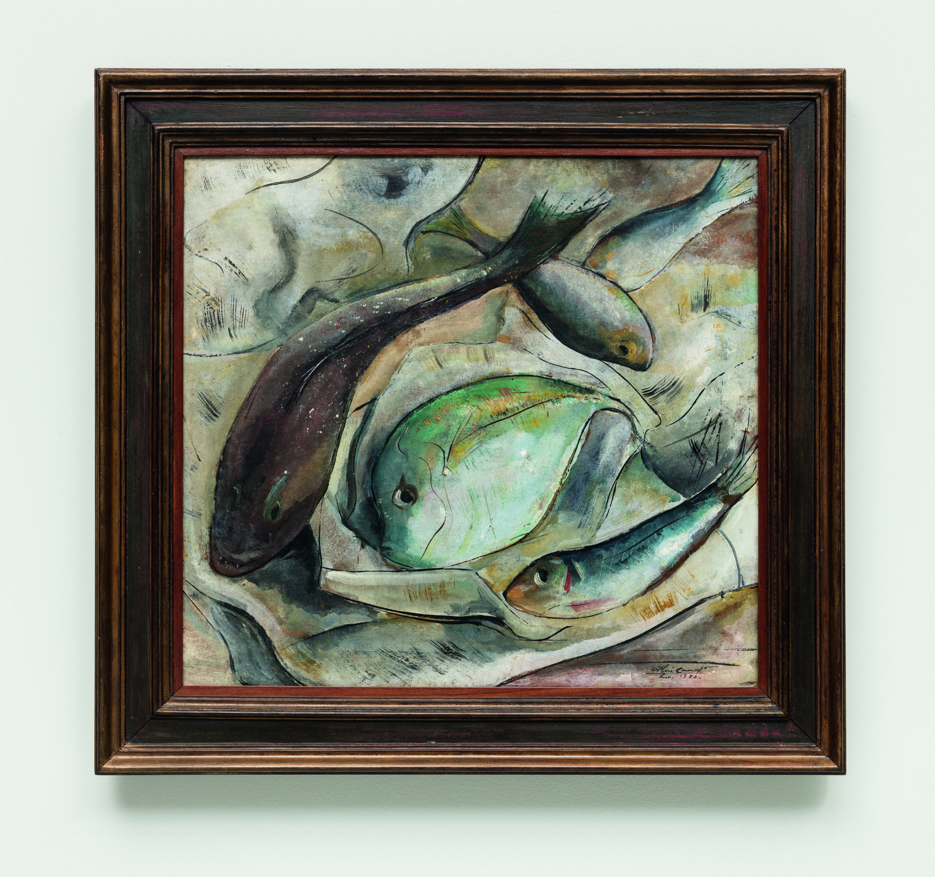 Descrição da imagem: Pintura de cinco peixes sobre um saco de papel. À esquerda, visto de cima, há um peixe marrom comprido, curvado na diagonal. No centro, visto de perfil, um peixe verde-água arredondado voltado para a esquerda. À direita, um peixe menor cinza. Os outros dois peixes estão na parte superior direita, um deitado sobre a cabeça do outro. No canto inferior direito, há uma pequena assinatura em preto: Iberê Camargo. Rio Mil novecentos e quarenta e três. A moldura é grossa e marrom. Fim da descrição. 
