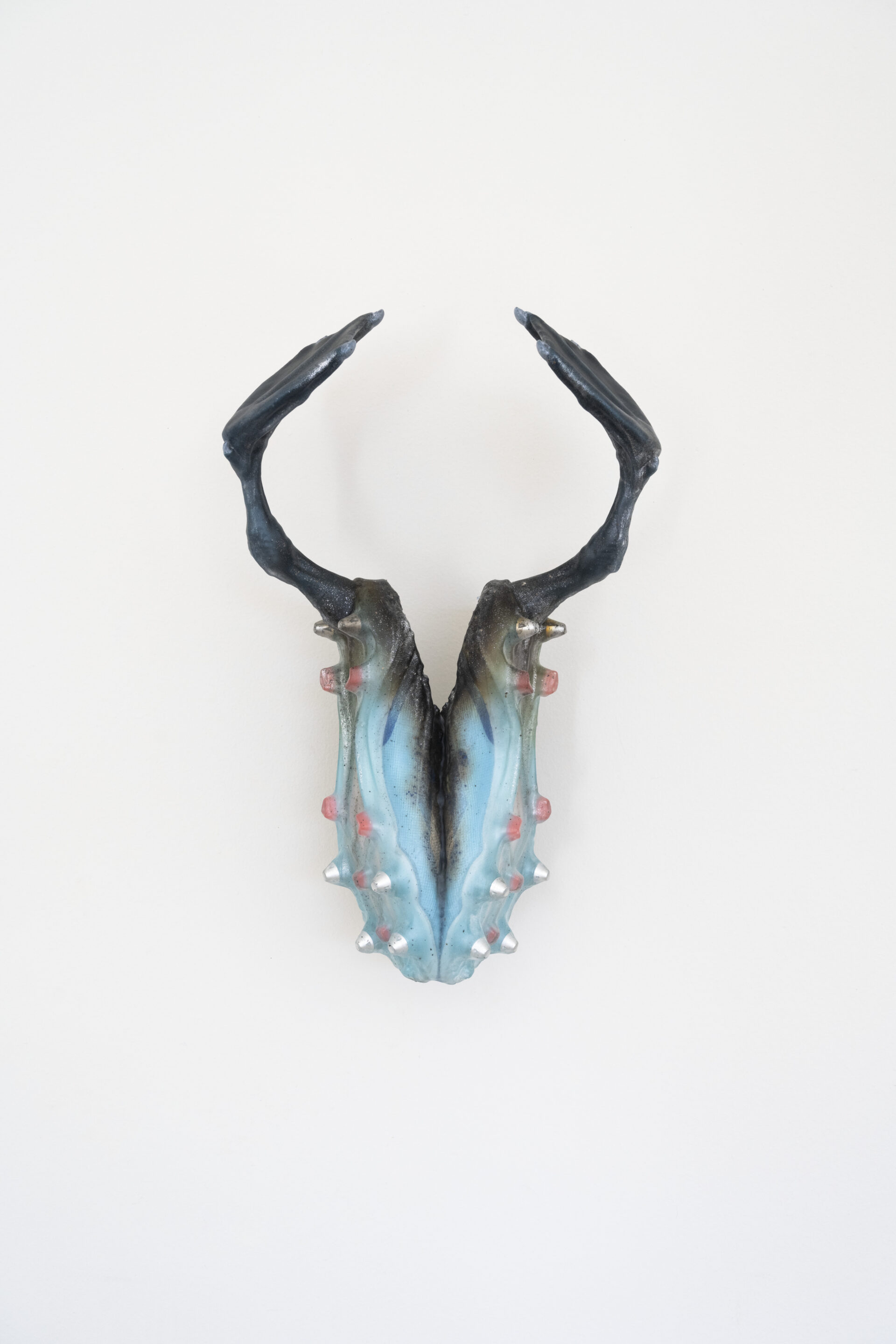 Descrição da imagem: Objeto construído por um par de chuteiras azuladas grudadas na vertical, pela parte interna. Os pinos da sola tem tons metálicos. De cada uma, sai um pé de cisne preto. O fundo é branco. Fim da descrição da imagem.