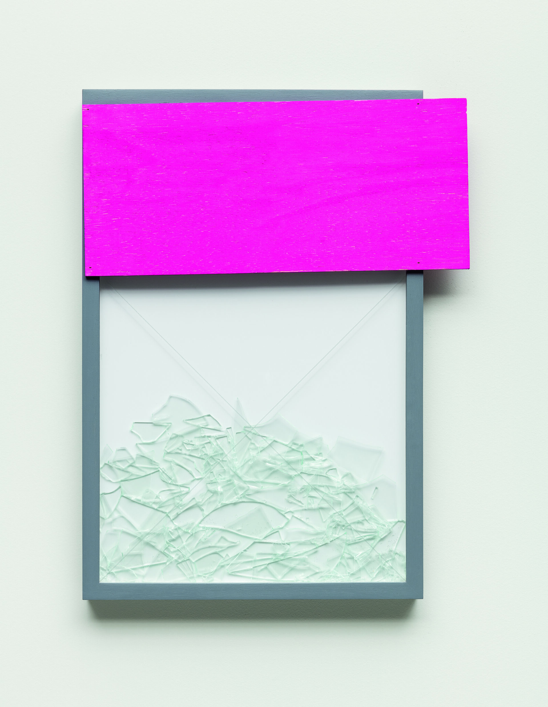 Descrição da imagem: Assemblage com cacos de vidro. Em um quadro vertical de moldura cinza, uma placa de madeira rosa horizontal está posicionada na parte superior. Vários cacos de vidro transparente de diversos tamanhos estão acumulados na base, sobre os quais duas linhas finas brancas se cruzam em X. Fim da descrição. 
