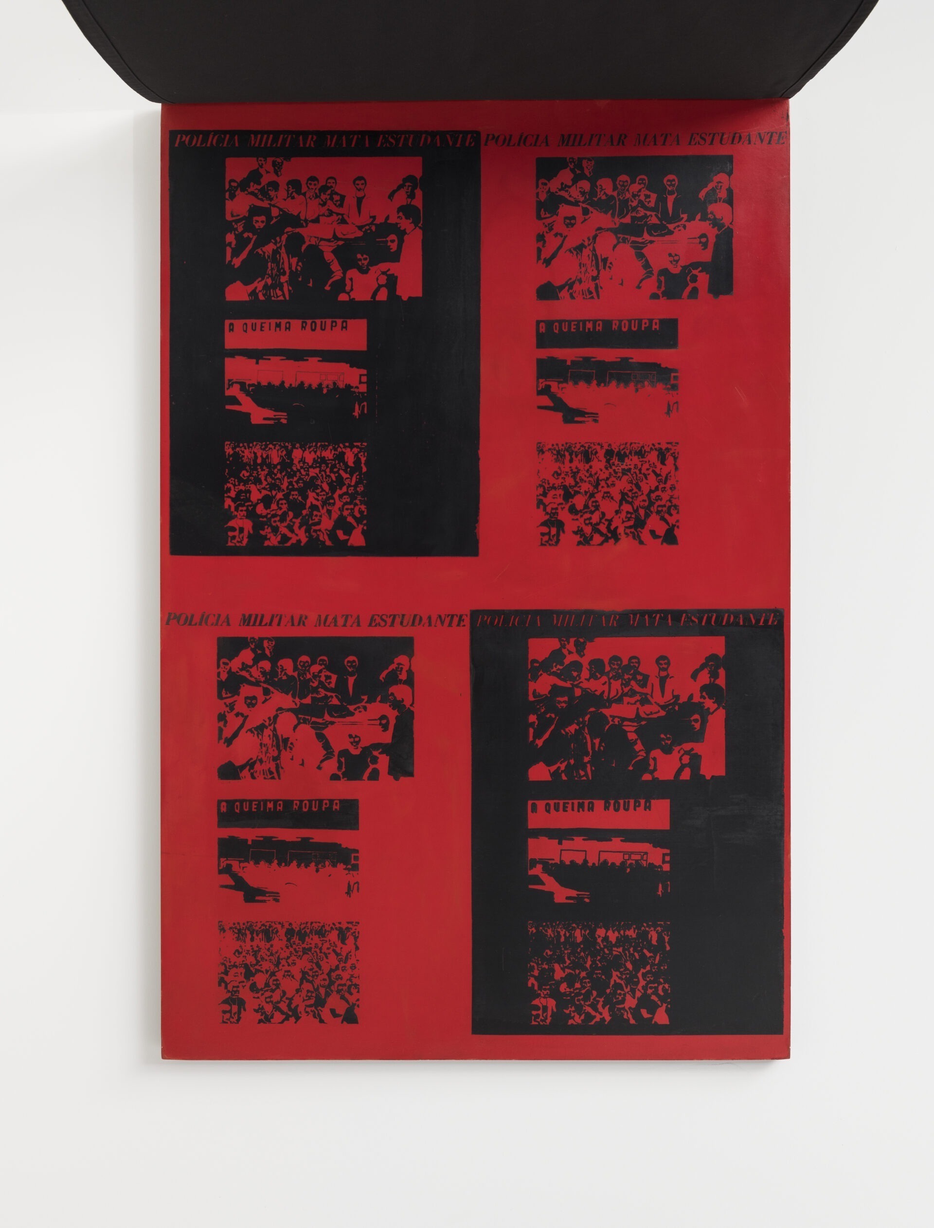 Descrição da imagem: Mesma obra da fotografia anterior. a obra está aberta: sobre a superfície de madeira pintada de vermelho, quatro quadrantes de serigrafias repetem as frases 'Polícia militar mata estudante' e 'A queima roupa', acompanhadas por figuras em preto de aglomerações de pessoas. Fim da descrição. 
