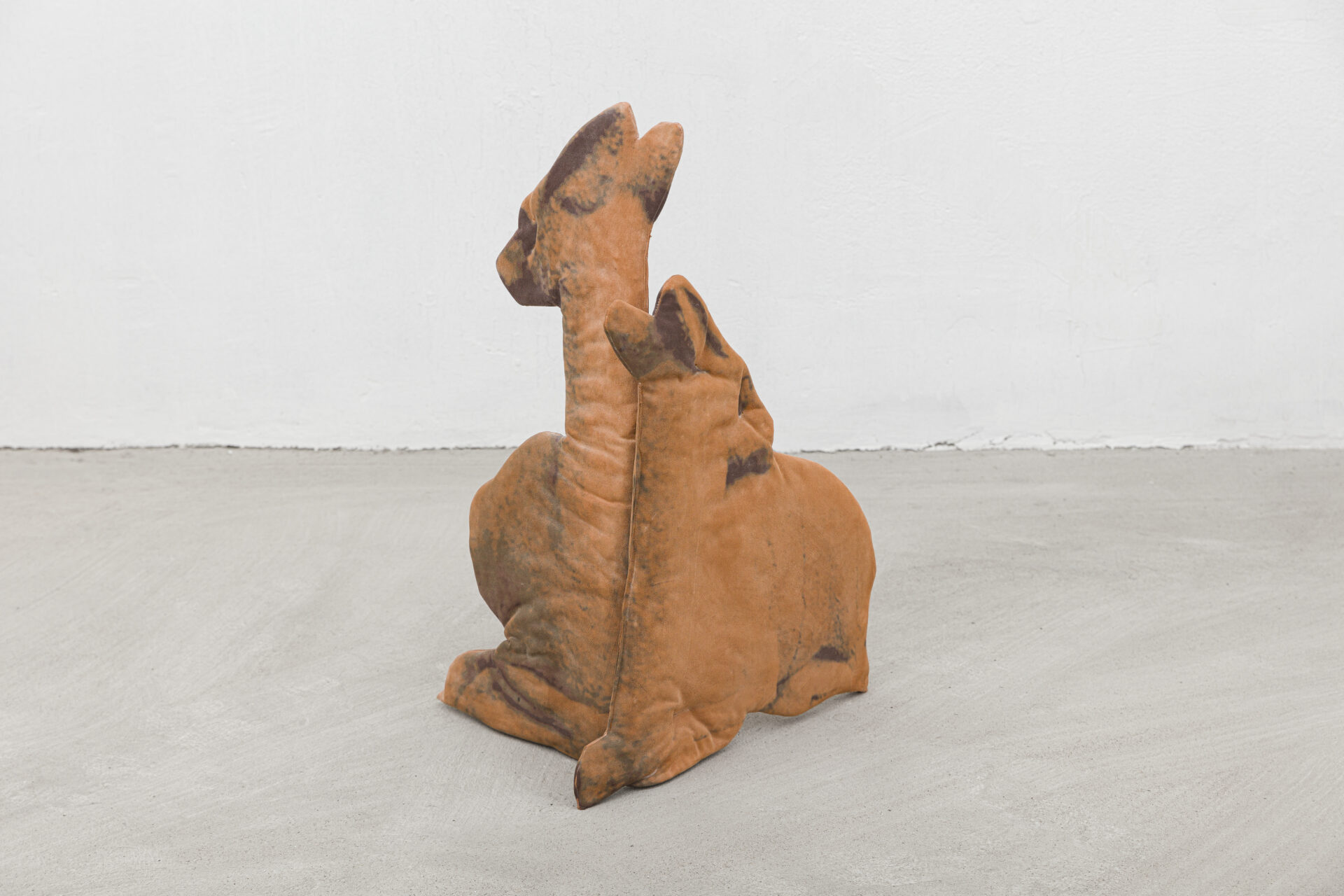 Descrição da imagem: Escultura de dois veados marrom-alaranjados vistos de frente. Estão sentados, com as patas dianteiras dobradas junto ao corpo, os corpos unidos, as cabeças viradas para trás e as orelhas erguidas. O pescoço de ambos é alongado: o veado à esquerda tem o pescoço mais longo, e o veado à direita tem o pescoço mais curto. Fim da descrição da imagem.