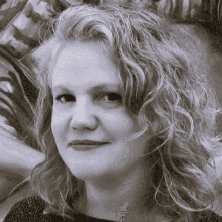 Imagem. Início da descrição de imagem: Retrato em close-up em tons de sépia ou preto e branco de uma mulher de pele clara e cabelos loiros ou grisalhos, ondulados e volumosos, que emolduram seu rosto. Ela tem uma expressão suave, com os lábios levemente marcados, e veste uma peça de roupa escura. O fundo está desfocado, com texturas indistintas. Fim da descrição de imagem.